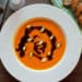 A top shot photo of Pumpkin Soup with nutmeg, pumpkin oil and pumpkin seeds served with some wholegrain bread