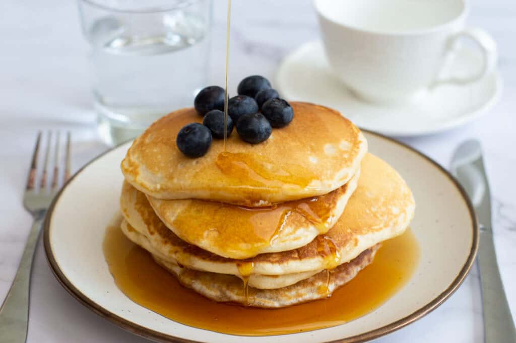American Pancakes with blueberries with maple syrup being drizzled on top