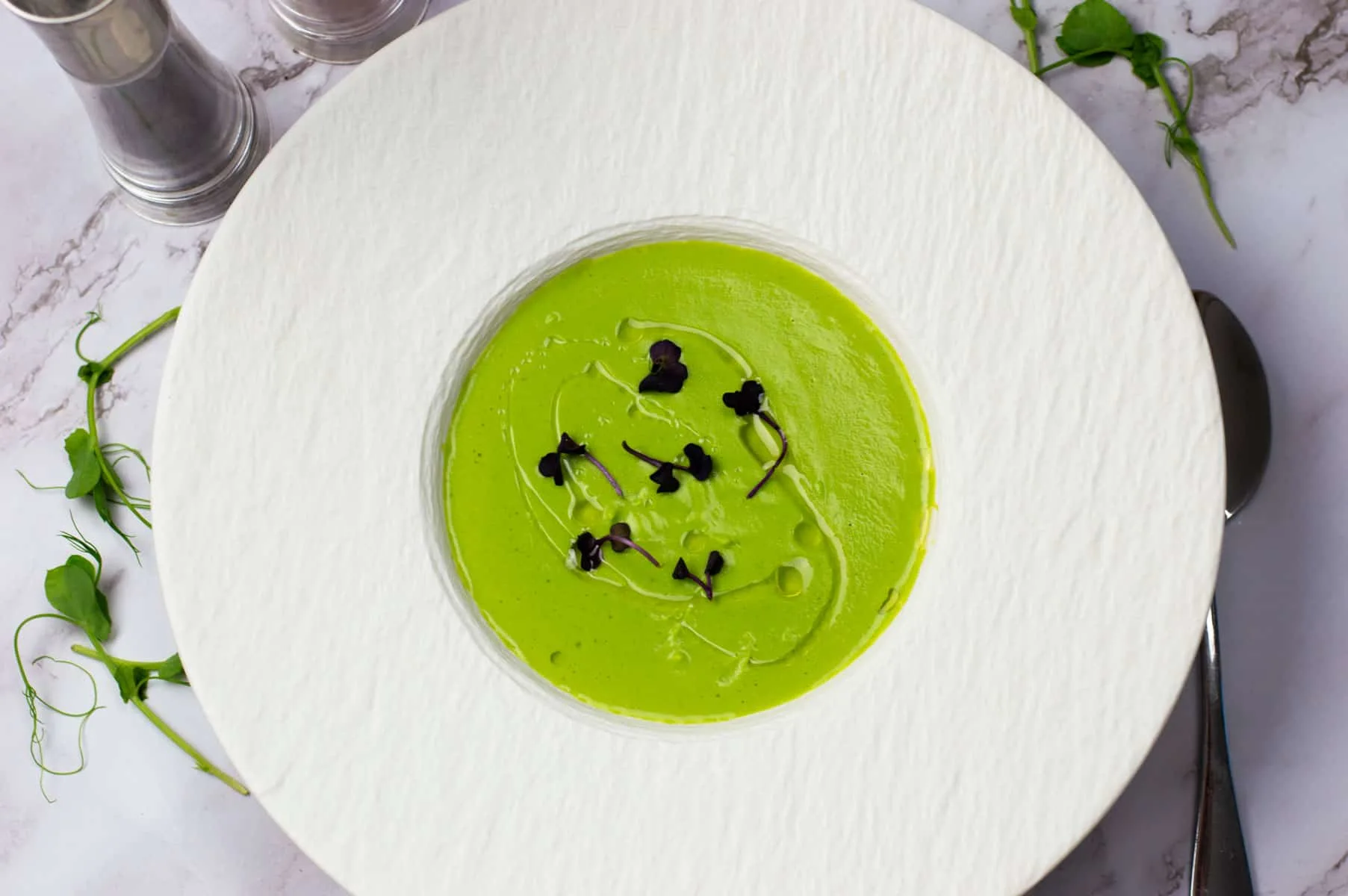 Pea soup with white truffle oil in a white bowl garnished with micro herbs