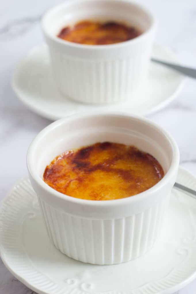 Two creme brulees in white ramekins on white plates