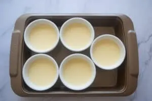 six ramekins of creme brulee in a baking tray