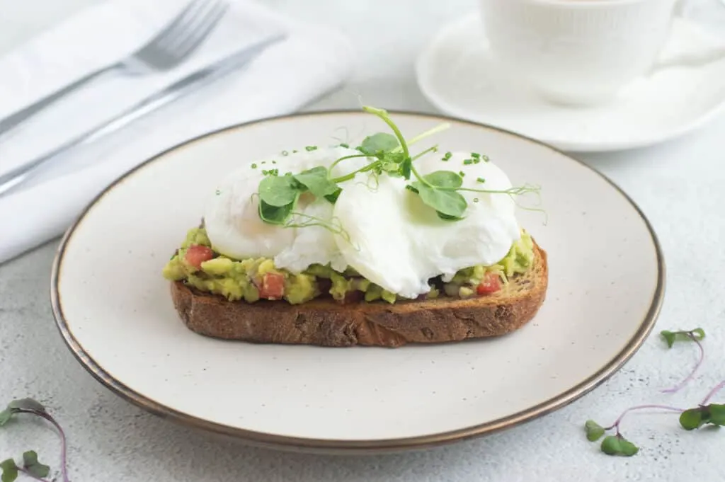 Poached eggs on toast with smacked avocado garnished with chives and pea shoots