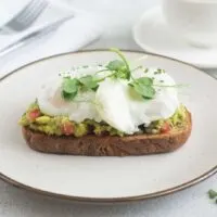 Poached eggs on toast with smacked avocado garnished with chives and pea shoots