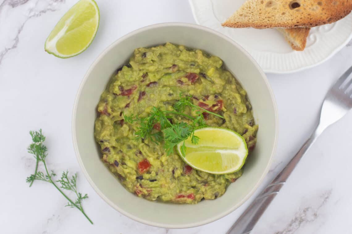 A bowl of smashed avocado with toast on the side