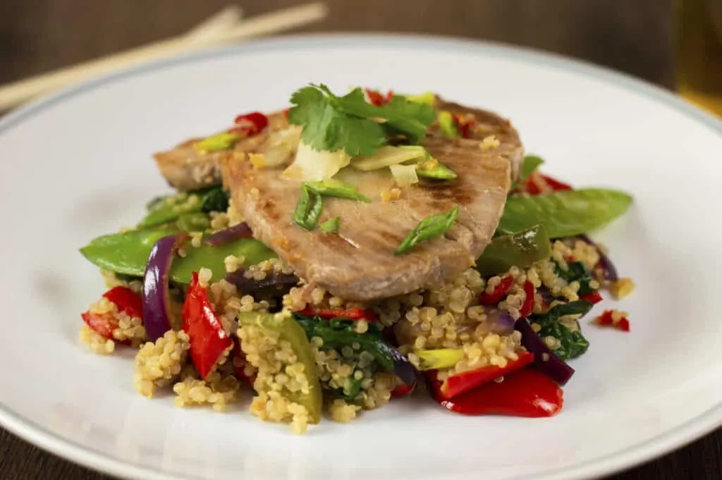 A plate of Seared Tuna steak on a pile of quinoa and stir-fried vegetables