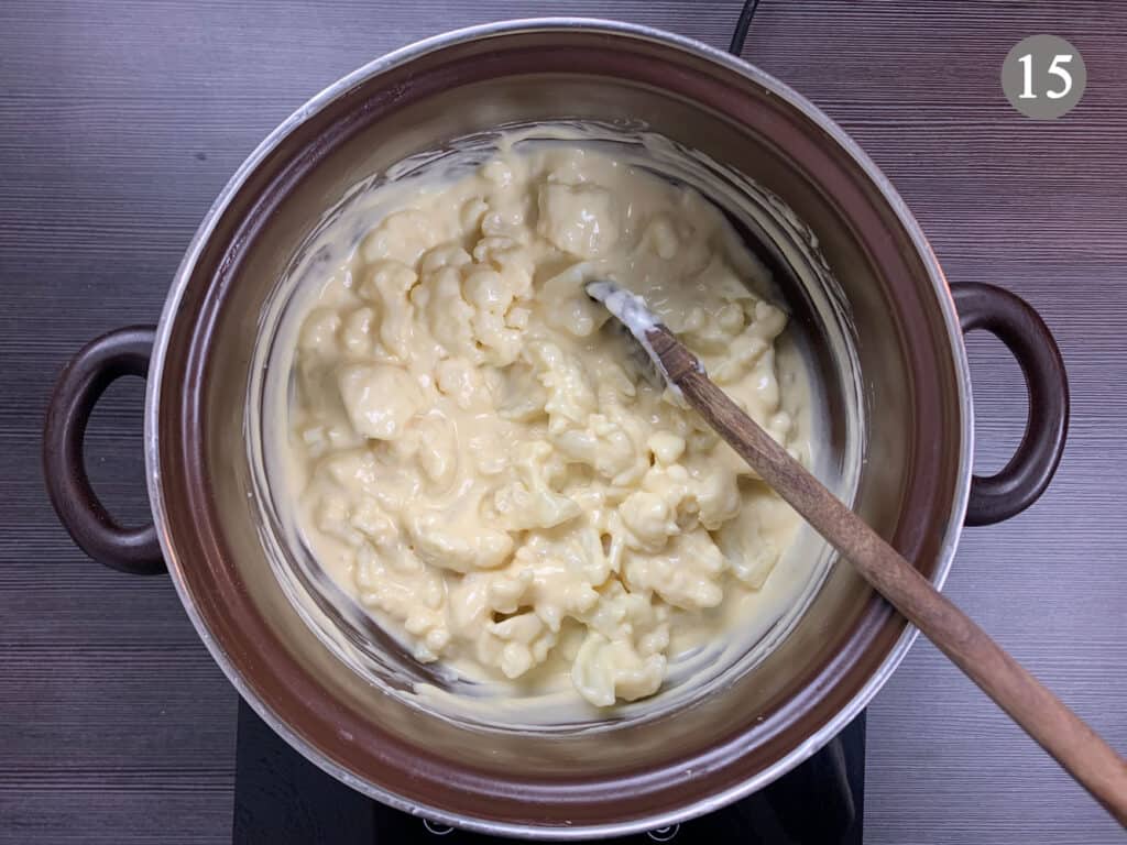 Mixing cauliflower into a pot of cheese sauce with a wooden spoon