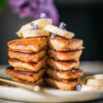 Buckwheat banana pancakes stacked on a plate, with banana as garnish. With a section cut into the pancakes showing the middle