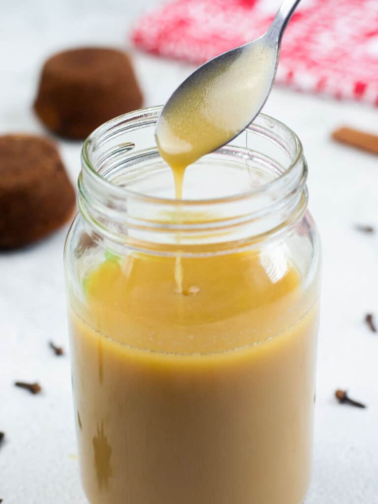 A spoon drizzling toffee sauce into a jar filled with toffee sauce