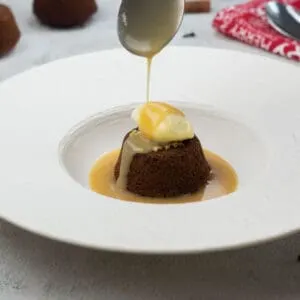 Sticky toffee pudding with spiced toffee sauce and ice cream. With spiced toffee sauce being drizzled onto the sticky toffee pudding.