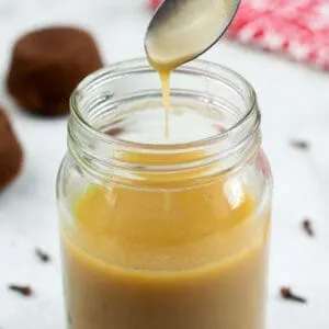 Toffee Sauce in a glass jar with spices and sticky toffee pudding in the background