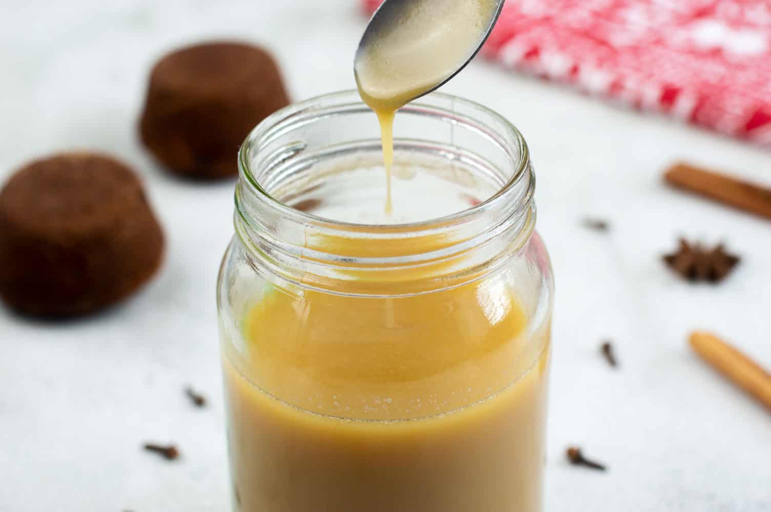 Toffee Sauce in a glass jar with spices and sticky toffee pudding in the background