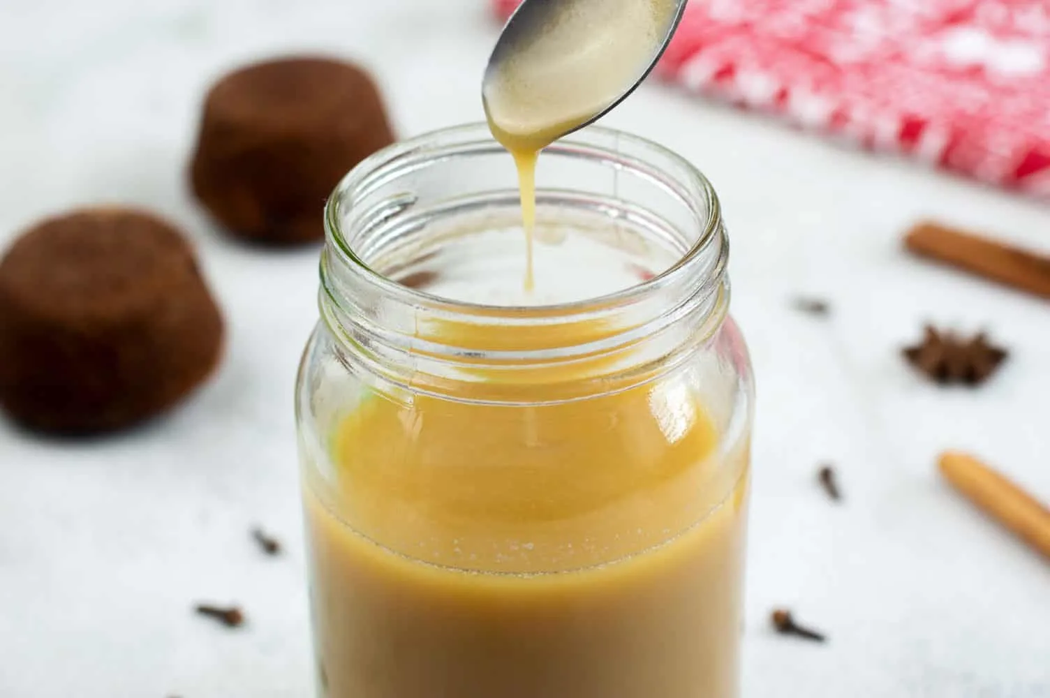 Toffee Sauce in a glass jar with spices and sticky toffee pudding in the background