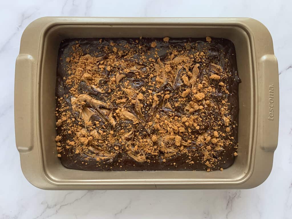 Biscoff brownie batter in a baking tray sprinkled with biscoff cookies