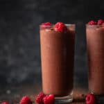 Chocolate, raspberry protein shake in a glass with lots of raspberries in the background