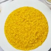 A plate of riso allo zafferano (saffron risotto) with saffron and parmesan cheese in the background
