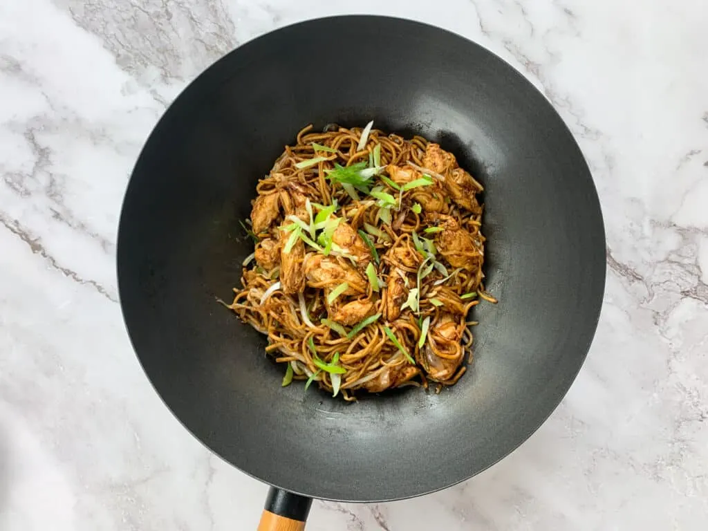 Finished Chow Mein in a large black wok, sprinkled with spring onions