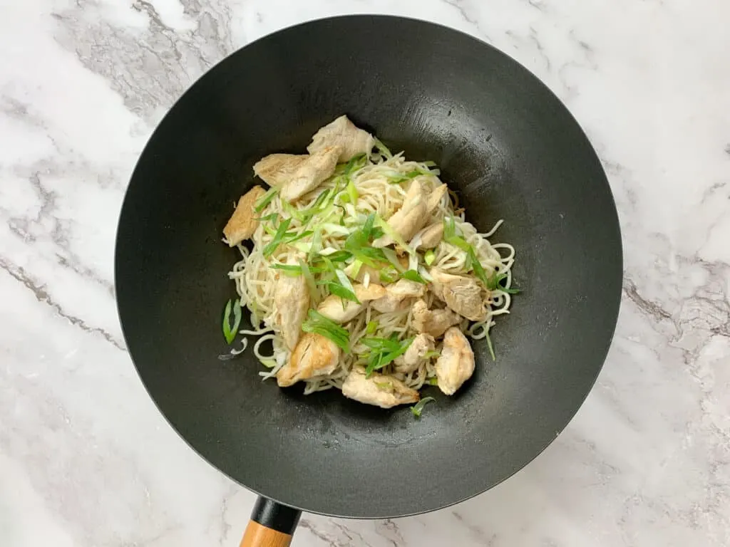 Adding noodles, chicken and bring onions into the wok