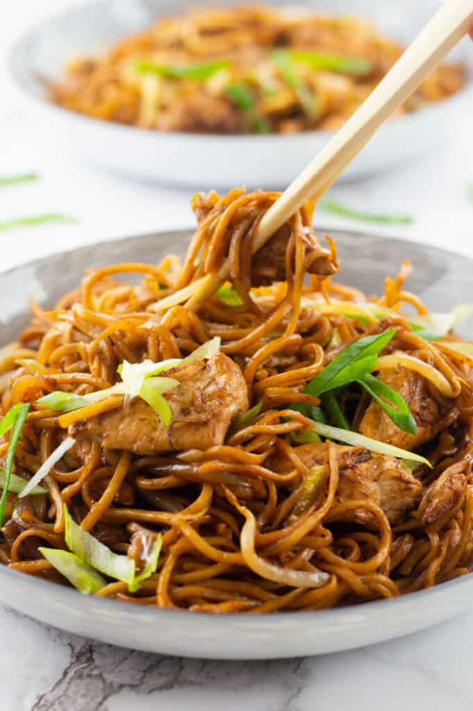 Two bowls of Chicken Chow Mein, with chop sticks grabbing a piece of chicken out of one