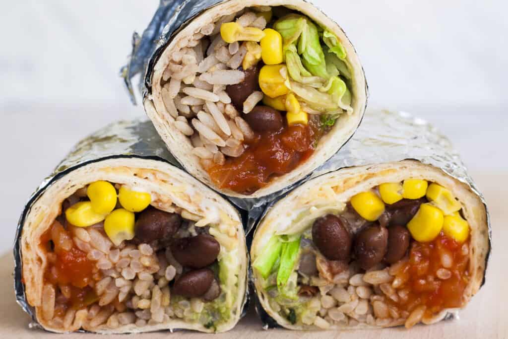 Three Chipotle inspired ingredients like black beans, cilantro lime rice, fajita veggies rolled into burritos