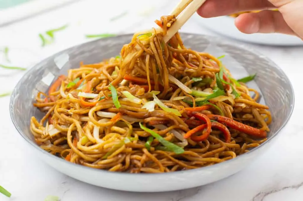 Chop sticks picking up some noodles from a bowl of vegetable chow mein