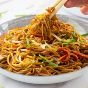 Chop sticks picking up some noodles from a bowl of vegetable chow mein
