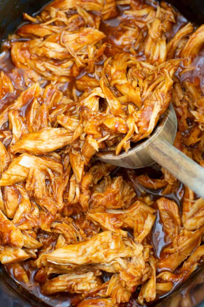 A wooden spoon mixing a crockpot of pulled bbq chicken