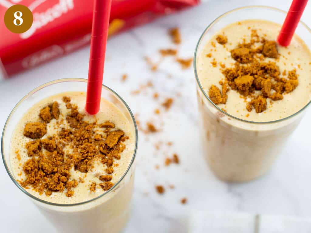 Two biscoff milkshakes in two tall glasses with a sprinkle of biscuits on top