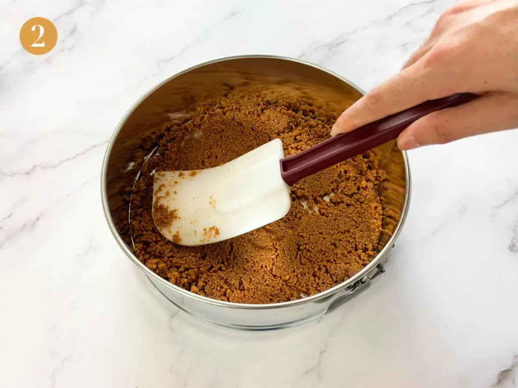 Patting down a biscoff crumb into the bottom of a cake tin