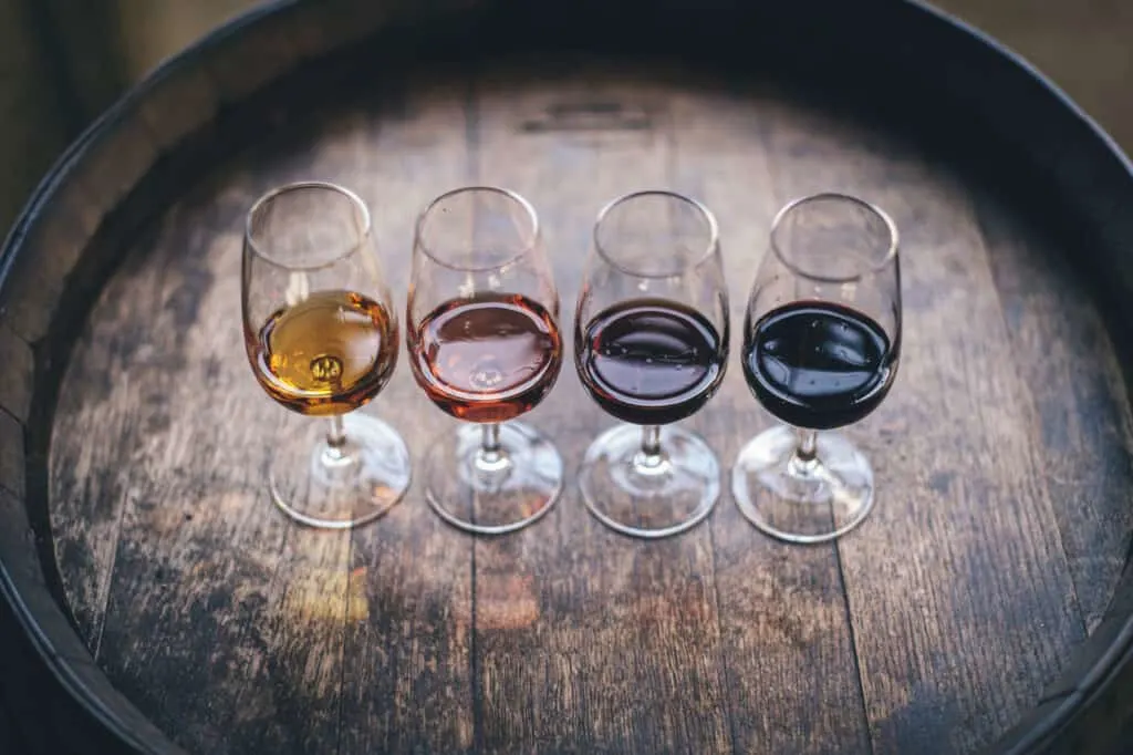 Red wine vinegar, red wine, sherry vinegar and white wine vinegar in glasses on a oak barrel