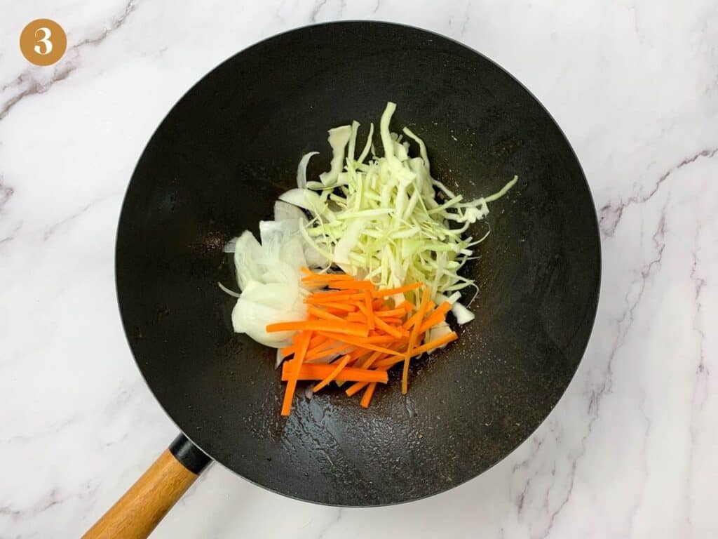 Sliced cabbage, carrots and onions in a large wok