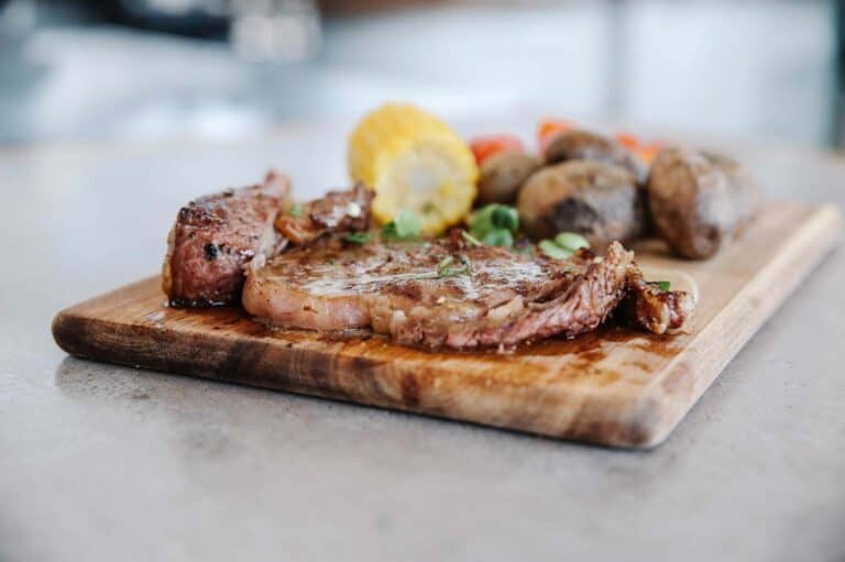 Grilled skirt steak, corn on the cob, baked potatoes and herbs on a wooden chopping board