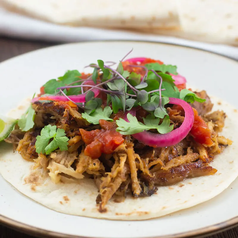 Taco de carnitas with salsa, herbs and pickled red onion topping