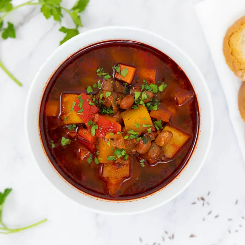 Vegan goulash garnished with parsley in a bowl with a side of bread