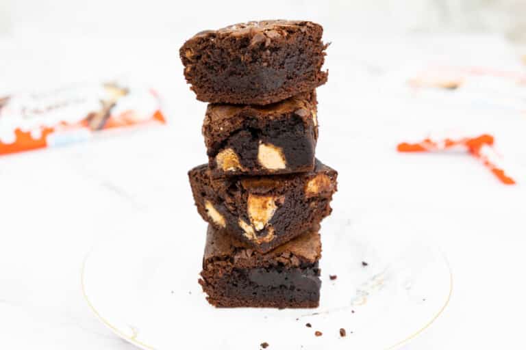 Four Kinder Bueno brownies stacked in a pile on a marble design plate with kinder buenos and kinder chocolate in the background