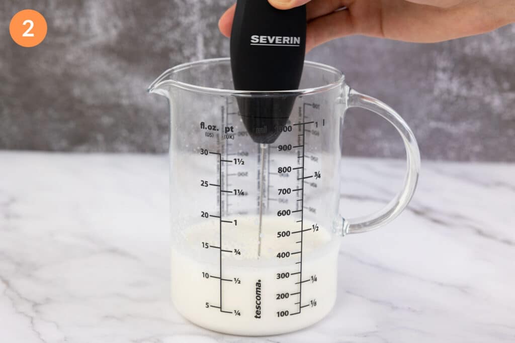 Foaming a jug of salted sweet cream with a milk frother