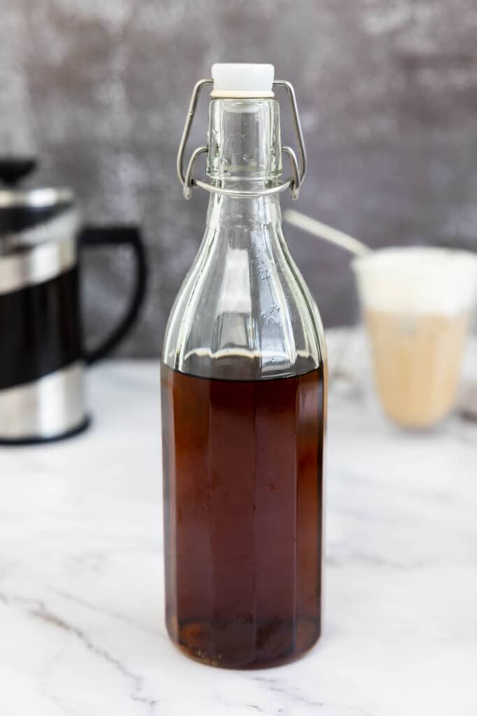 Starbucks vanilla syrup in a glass bottle in front of a french press and vanilla coffee