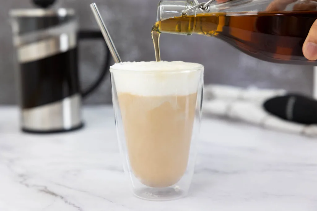 Pouring homemade starbucks vanilla syrup into a coffee which has a cold foam on top