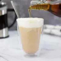 Pouring homemade starbucks vanilla syrup into a coffee which has a cold foam on top