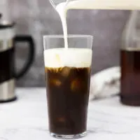 Pouring vanilla sweet cream cold foam into a glass of cold brew