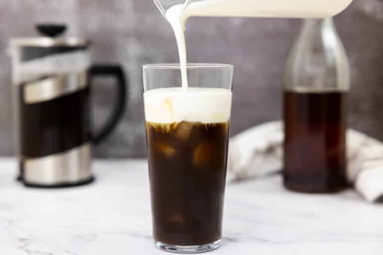 Pouring vanilla sweet cream cold foam into a glass of cold brew