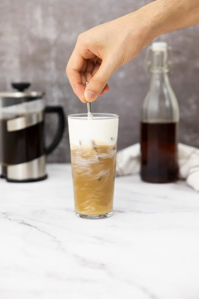 Vanilla sweet cream cold foam and ice brew in a glass being mixed with a reusable straw