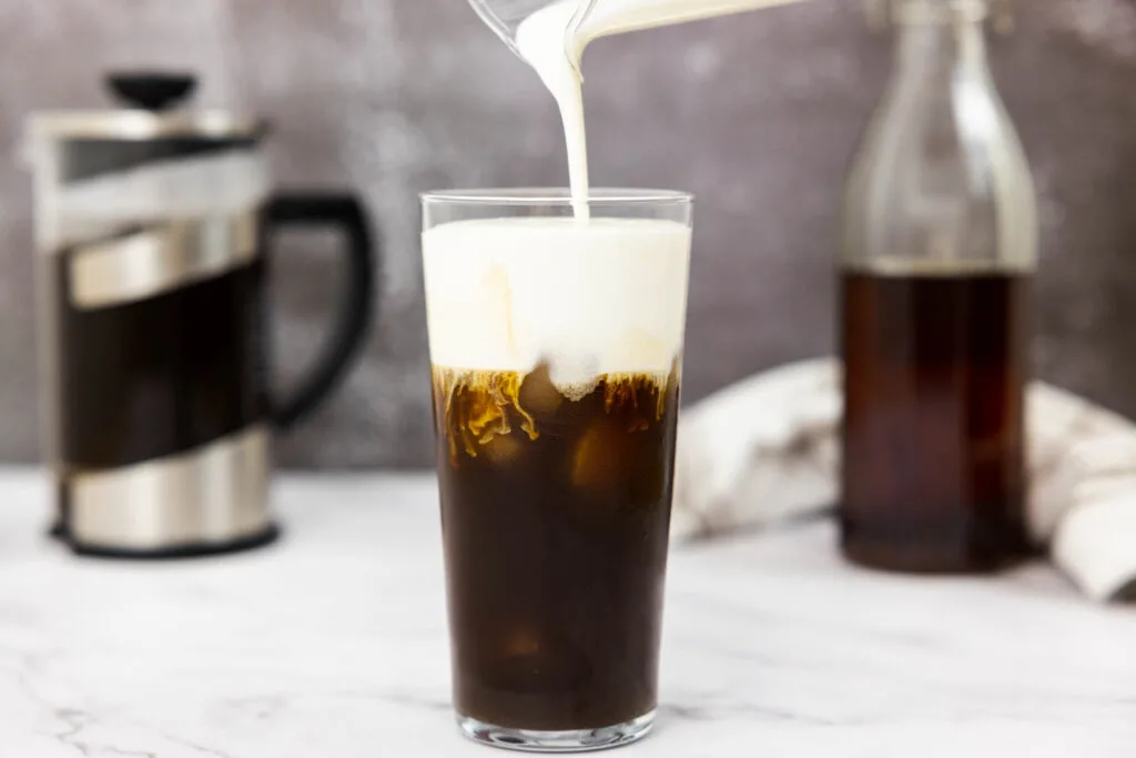 Pouring vanilla sweet cream cold foam into a glass of cold brew