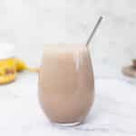 Weight gainer shake in a large glass with peanut butter and banana in the background