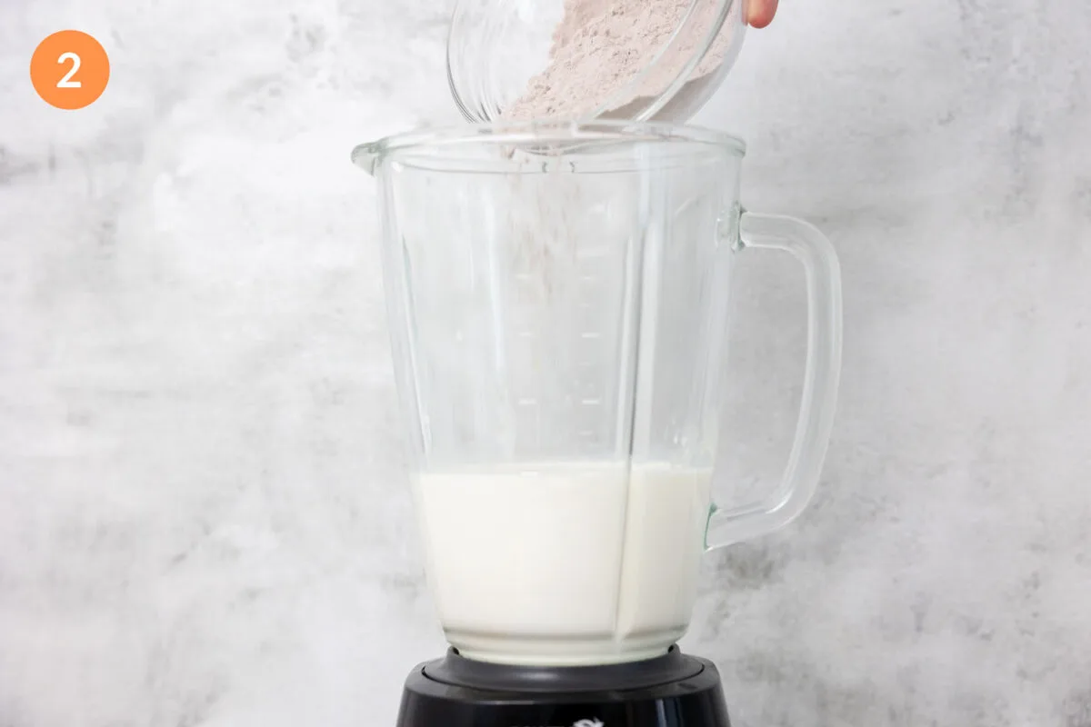 Pouring weight gainer protein powder into a large blender of milk