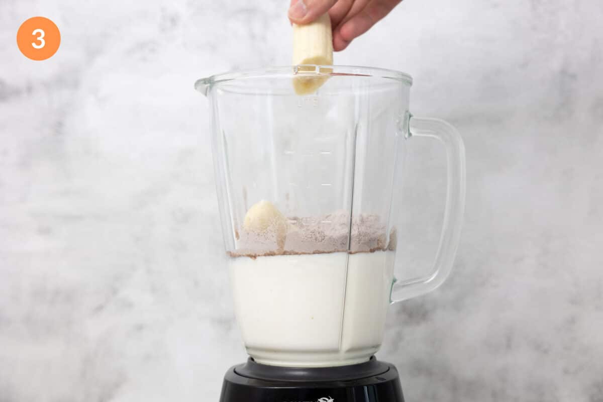 Adding banana into a blender of milk and weight gainer protein powder