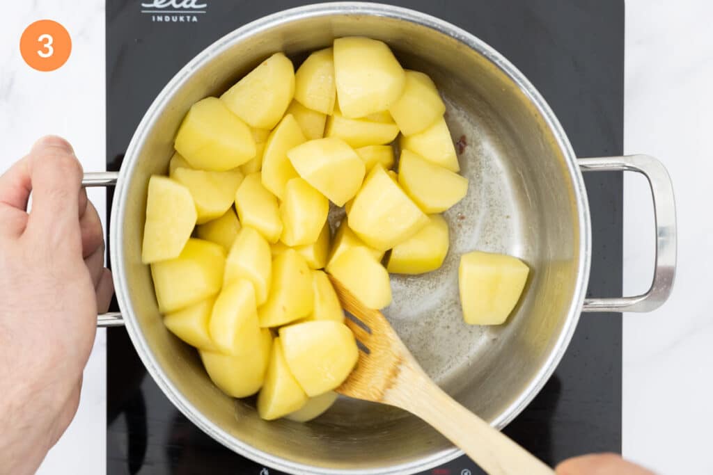 Chunks of potato being mixed through bacon fat in a large pot