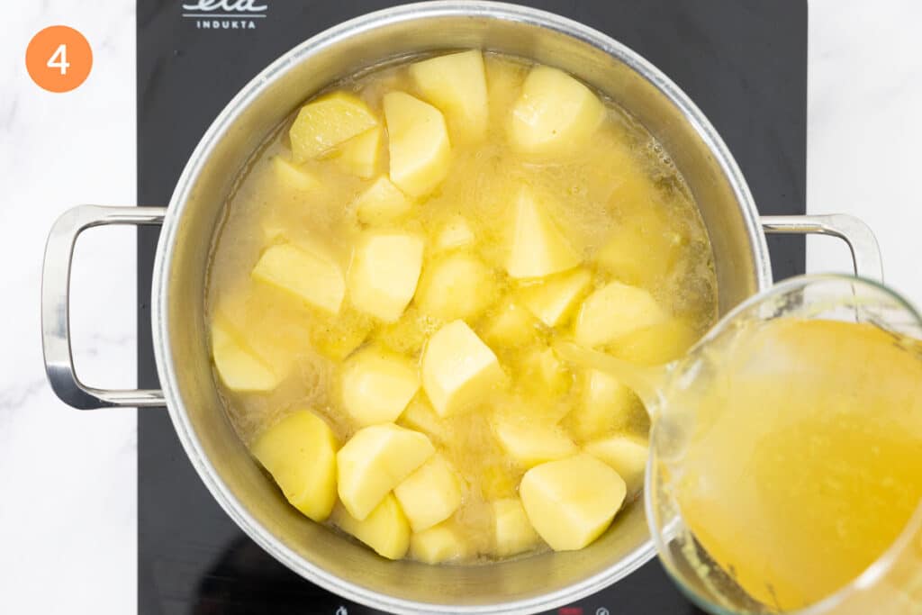Chicken stock being poured into a large pot of potatoes