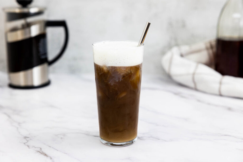 Cold foam on iced cold brew in a glass with a reusable straw
