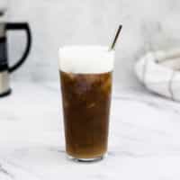 Cold foam on iced cold brew in a glass with a reusable straw