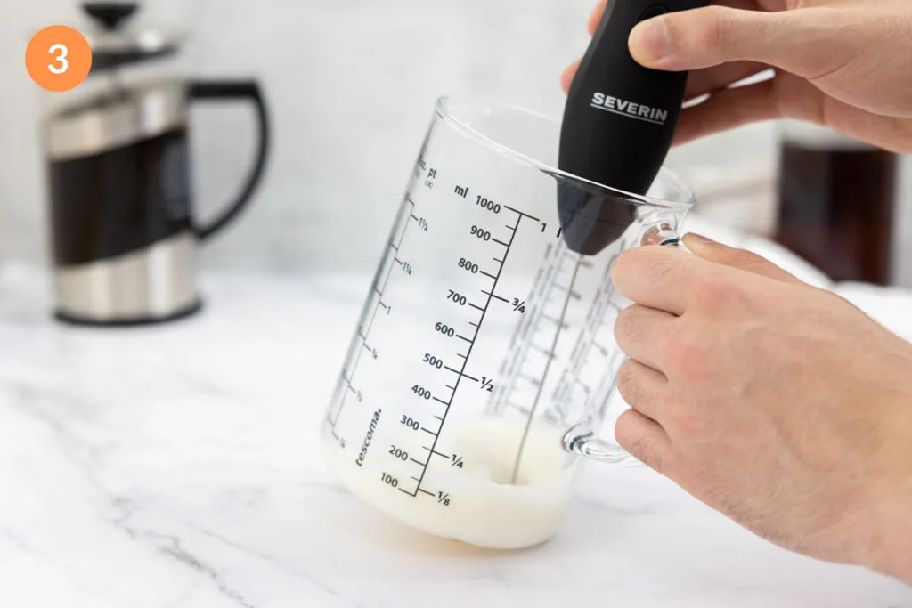 Foaming together milk and vanilla syrup in a jug with a electric foamer